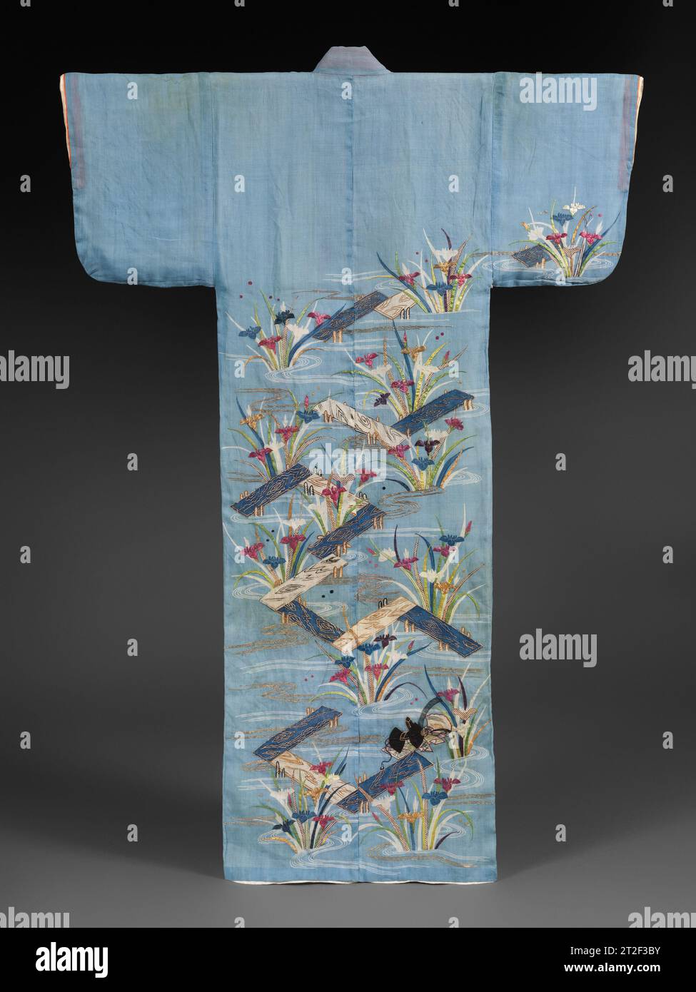 Summer Robe (Katabira) with Irises at Yatsuhashi Japan mid-19th century This samurai woman’s summer robe evokes water—light blue fabric with irises and zigzagging plank bridges. The composition refers to an episode from The Tales of Ise and the Noh play derived from it, Irises, in which an exiled ninth-century poet—alluded to on this robe by a courtier’s hat and a fan near the hem—and his friends leave the capital. Pausing at Yatsuhashi, where bridges cross eight channels of a river, they admire the irises growing in the riverbank. Inspired, the poet composes a poem in which each line begins w Stock Photo