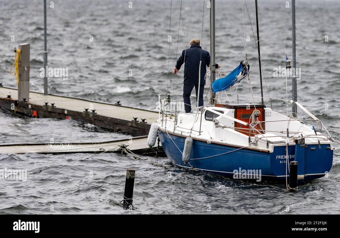 Kiel, Germany. 19th Oct, 2023. A man secures a sailboat at a jetty on