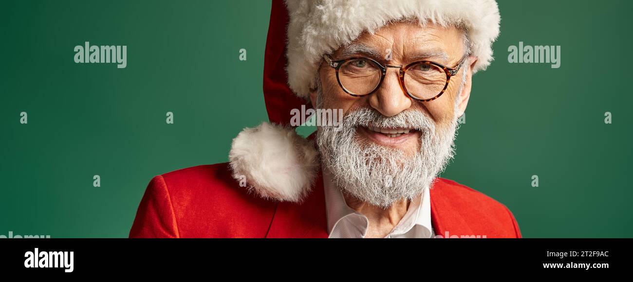 elegant handsome Santa in red hat and glasses smiling cheerfully at camera, winter concept, banner Stock Photo