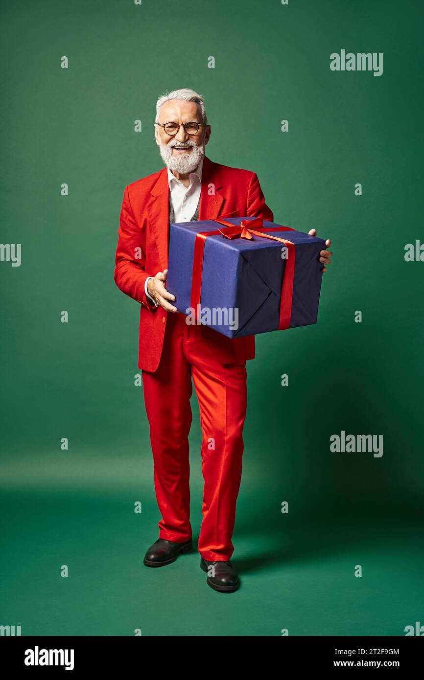 good looking man dressed like Santa posing with huge present on green backdrop, winter concept Stock Photo