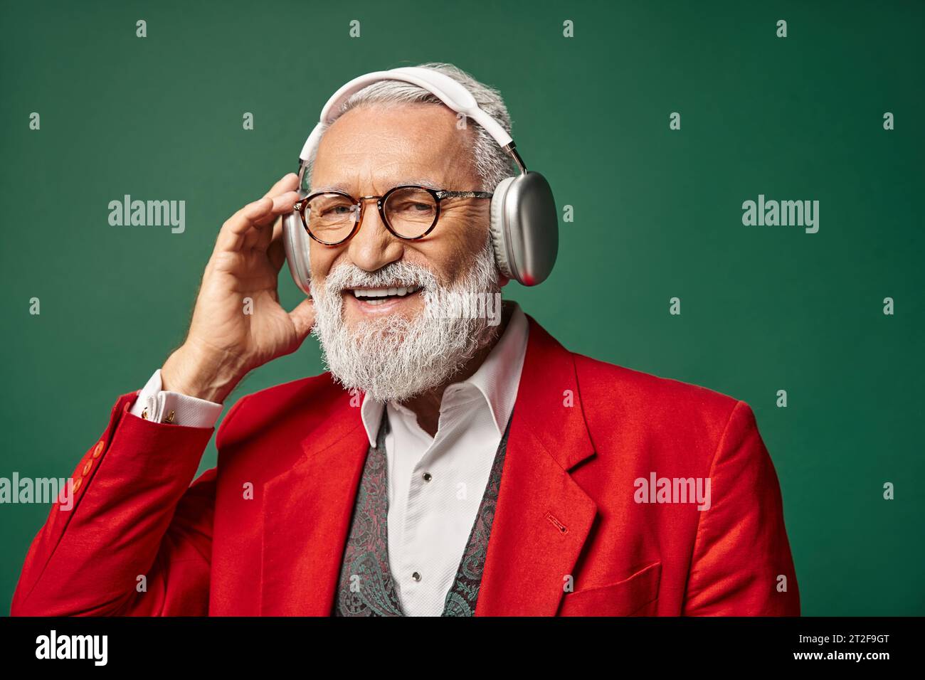 good looking elegant man in red Santa suit wearing headphones and smiling at camera, winter concept Stock Photo
