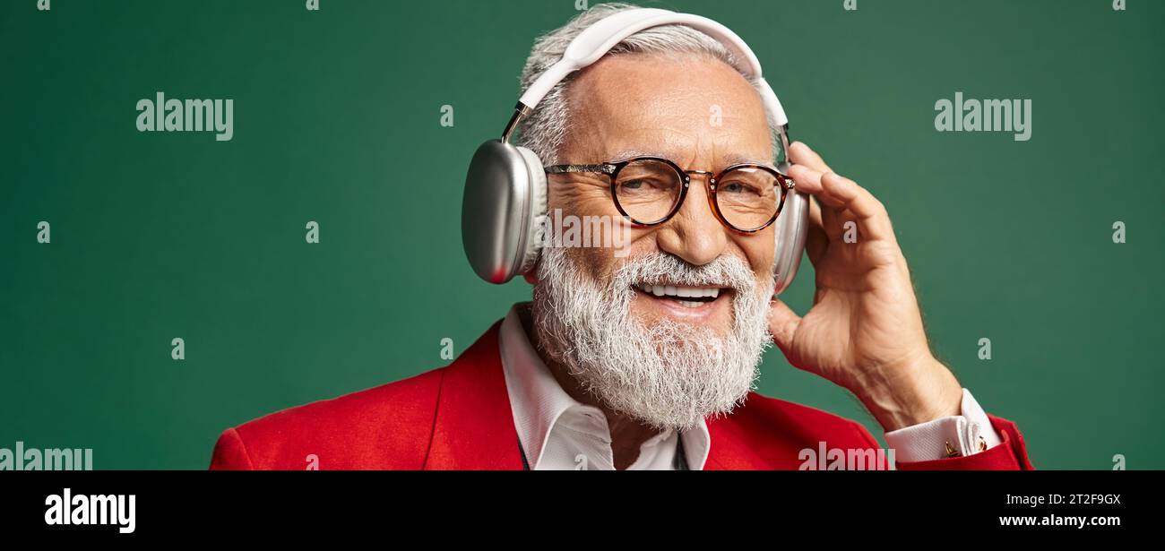 cheerful man dressed as Santa Claus with beard and headphones smiling at camera, winter, banner Stock Photo