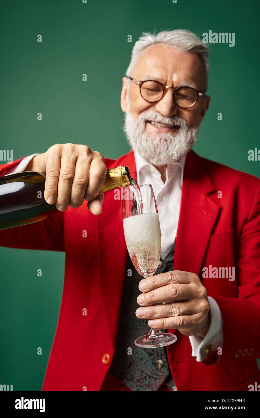 cheerful elegant Santa Claus pouring champagne into flute glass and smiling happily, winter concept Stock Photo