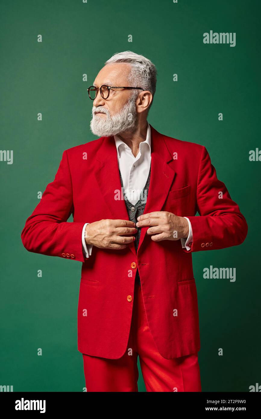handsome man dressed as Santa with glasses fastening buttons on suit looking away, winter concept Stock Photo