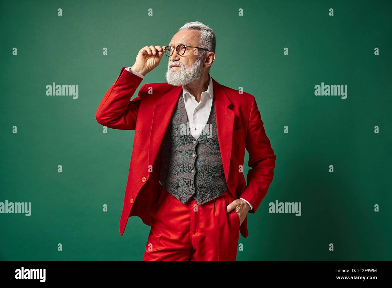 elegant Santa in red suit posing touching his glasses with one hand in pocket, Christmas concept Stock Photo