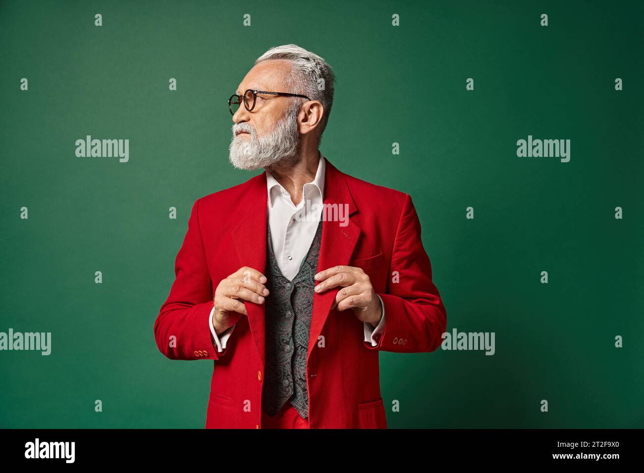 good looking elegant Santa with glasses touching his suit and looking away, winter concept Stock Photo