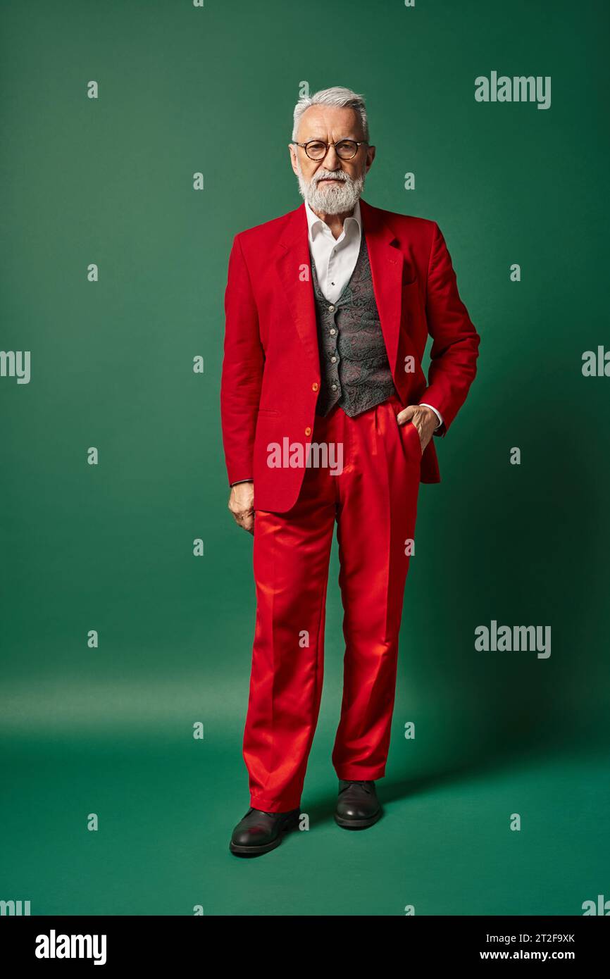 classy man dressed as Santa posing with one hand in pocket on green backdrop, winter concept Stock Photo