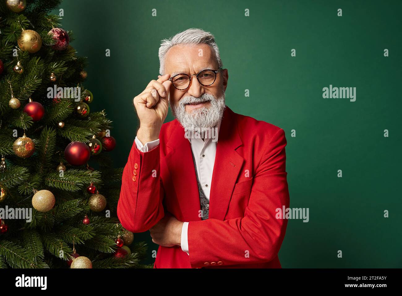 classy man dressed as Santa crossing arms and touching glasses next to fir tree, winter concept Stock Photo