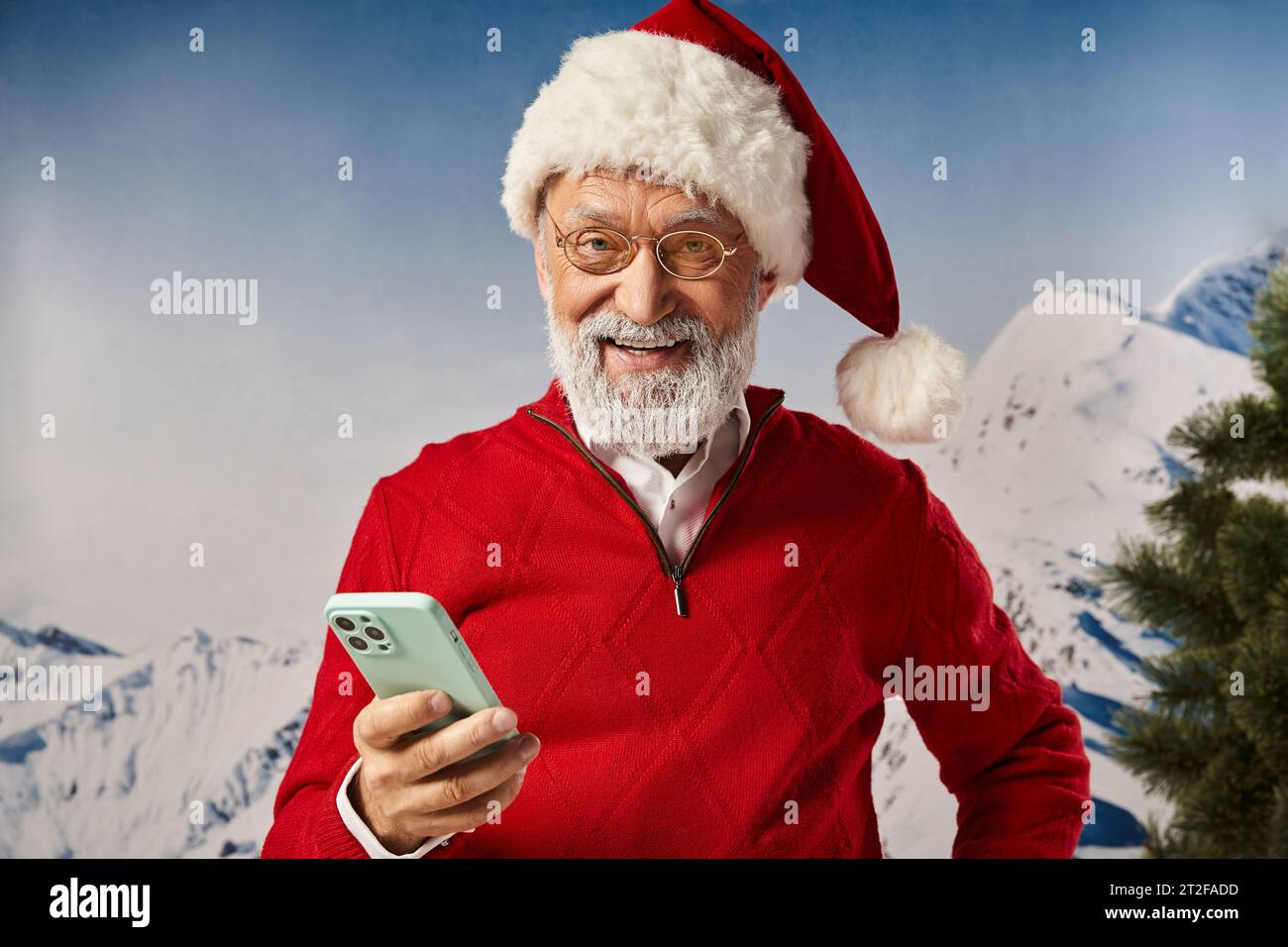 cheerful man in red Santa costume holding mobile phone and smiling at camera, winter concept Stock Photo