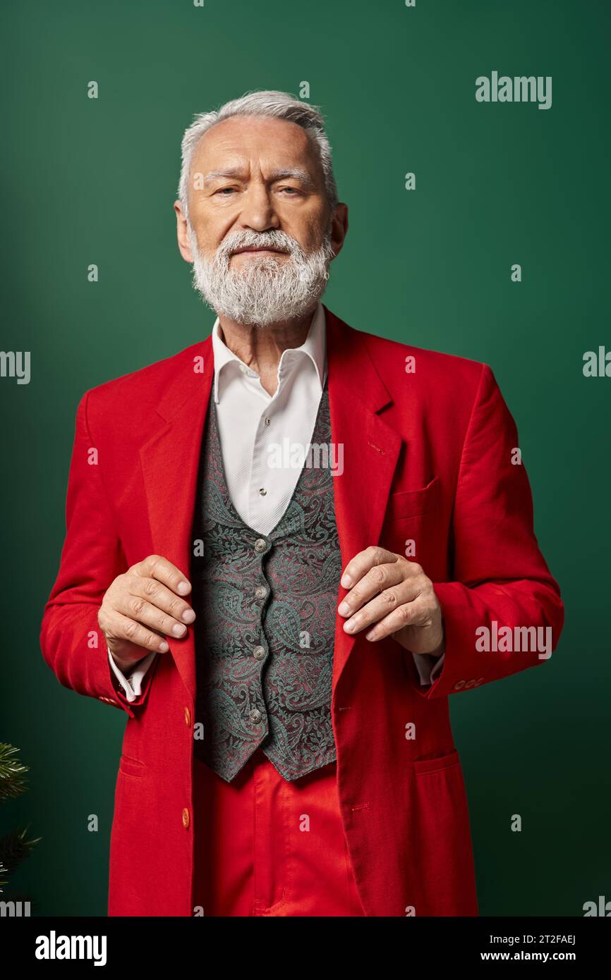 elegant white bearded Santa posing with hands on suit and looking at camera, winter concept Stock Photo