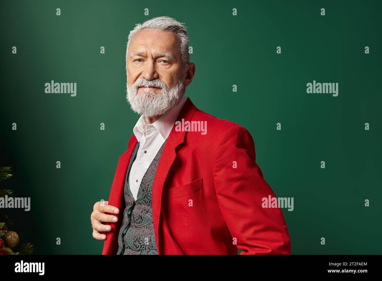 portrait of stylish man in red Santa suit looking at camera on green backdrop, winter concept Stock Photo
