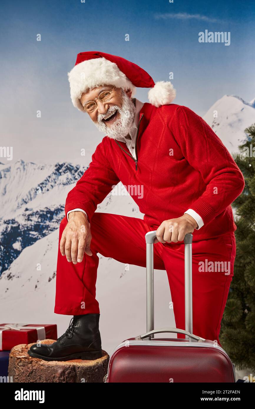 happy man in Santa costume with suitcase wearing glasses and smiling at camera, winter concept Stock Photo