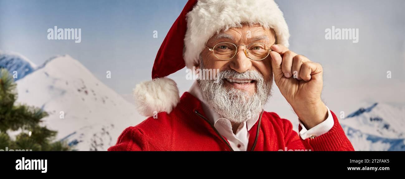 cheerful man in Santa costume with glasses on looking straight at camera, winter concept, banner Stock Photo