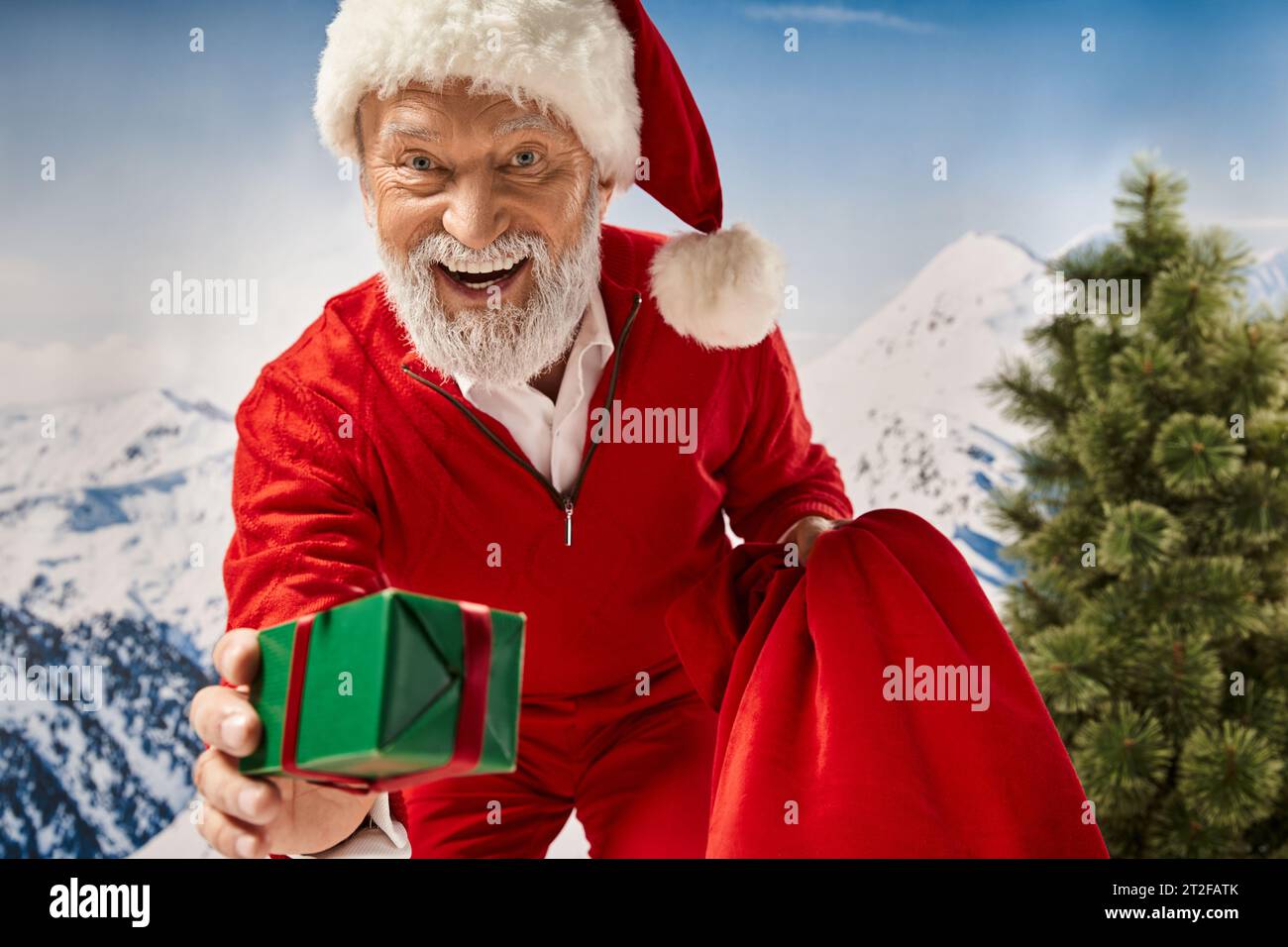 joyous man dressed as Santa lending present at camera and smiling cheerfully, winter concept Stock Photo