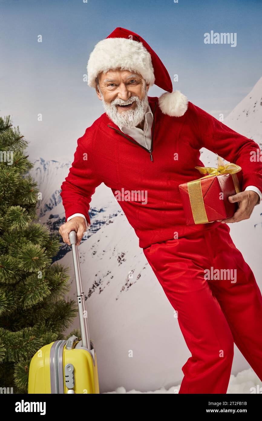 cheerful Santa costume with white beard posing with yellow suitcase and present, Christmas concept Stock Photo