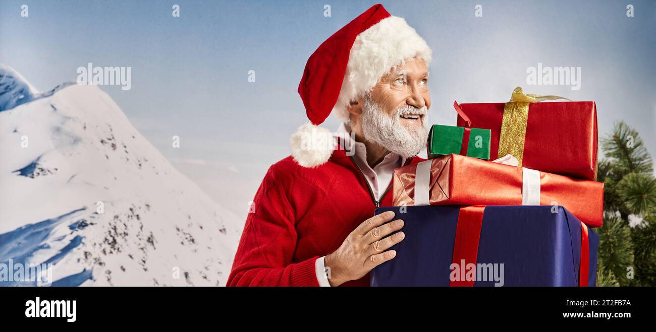 cheerful Santa with christmassy hat holding presents in hands looking away, winter concept, banner Stock Photo