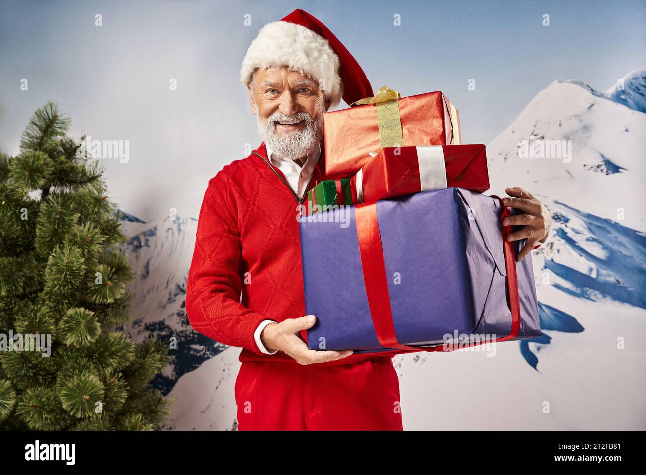 white bearded Santa holding of presents and smiling at camera with snowy backdrop, winter concept Stock Photo
