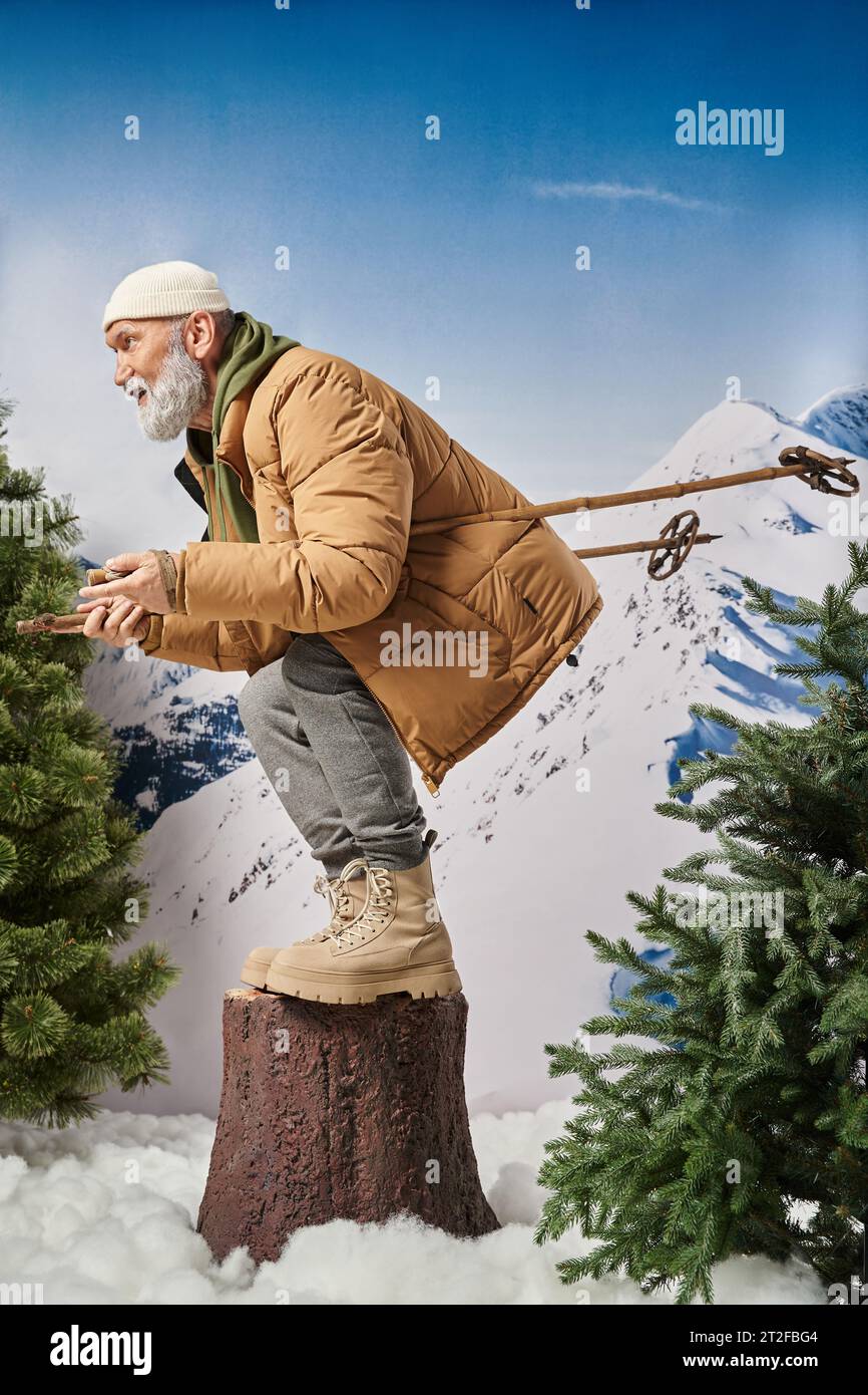 athletic Santa squatting with ski poles on tree stump with mountain backdrop, winter concept Stock Photo