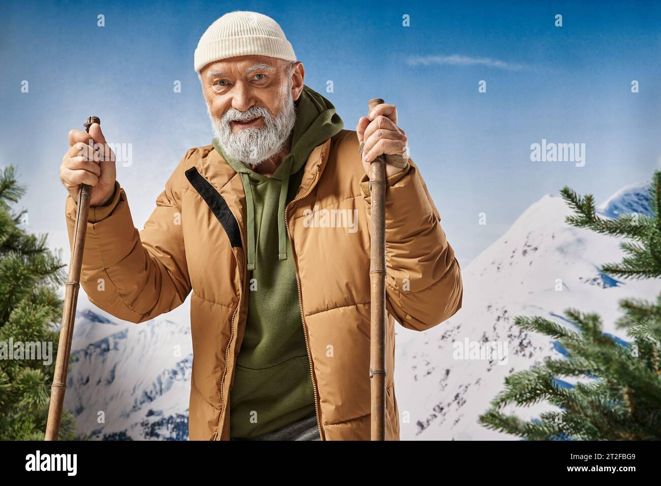 cheerful man standing on skis wearing white hat and jacket with mountains backdrop, winter concept Stock Photo