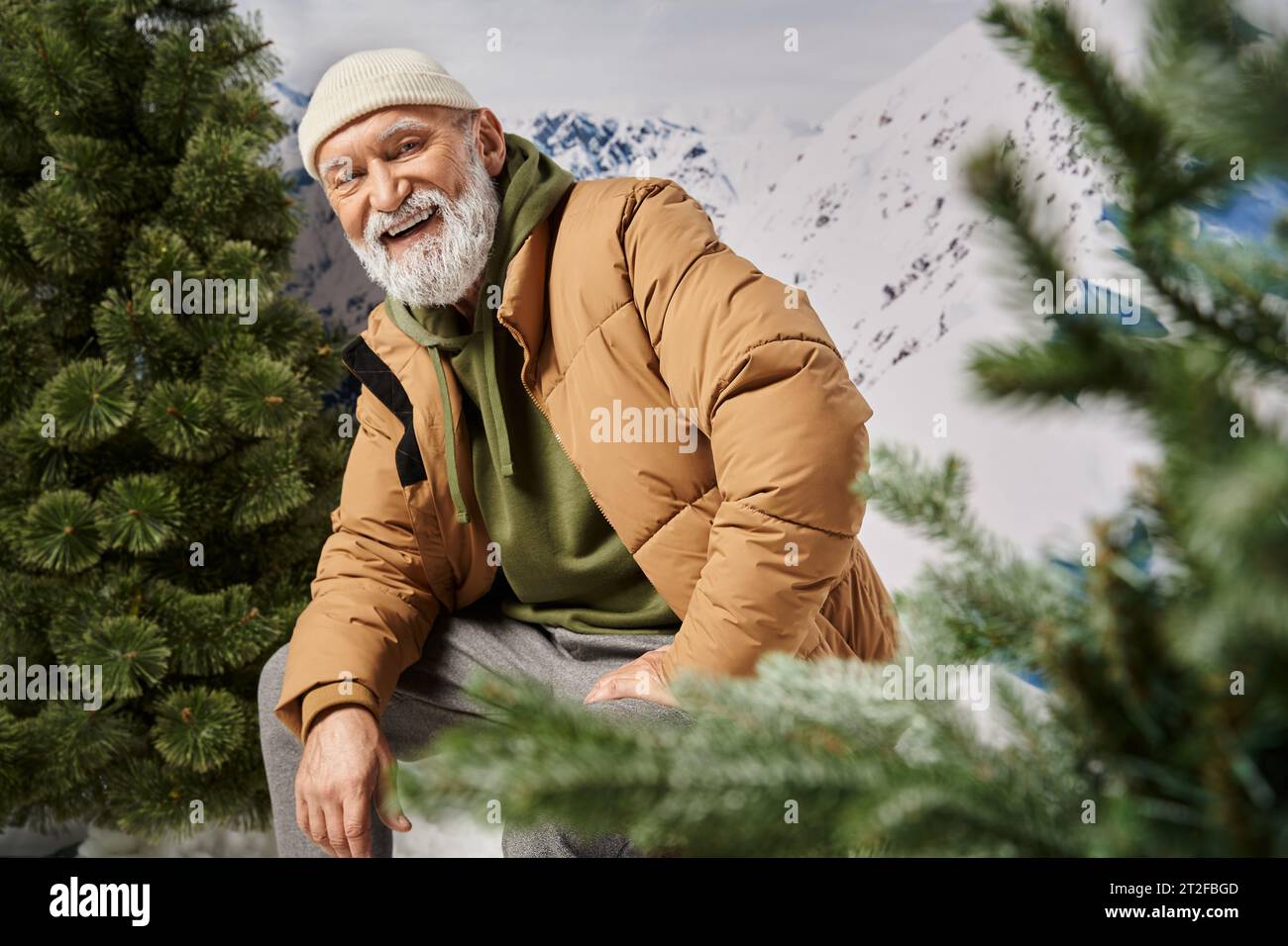 cheerful man dressed as Santa with white beard surrounded by trees and snow, winter concept Stock Photo
