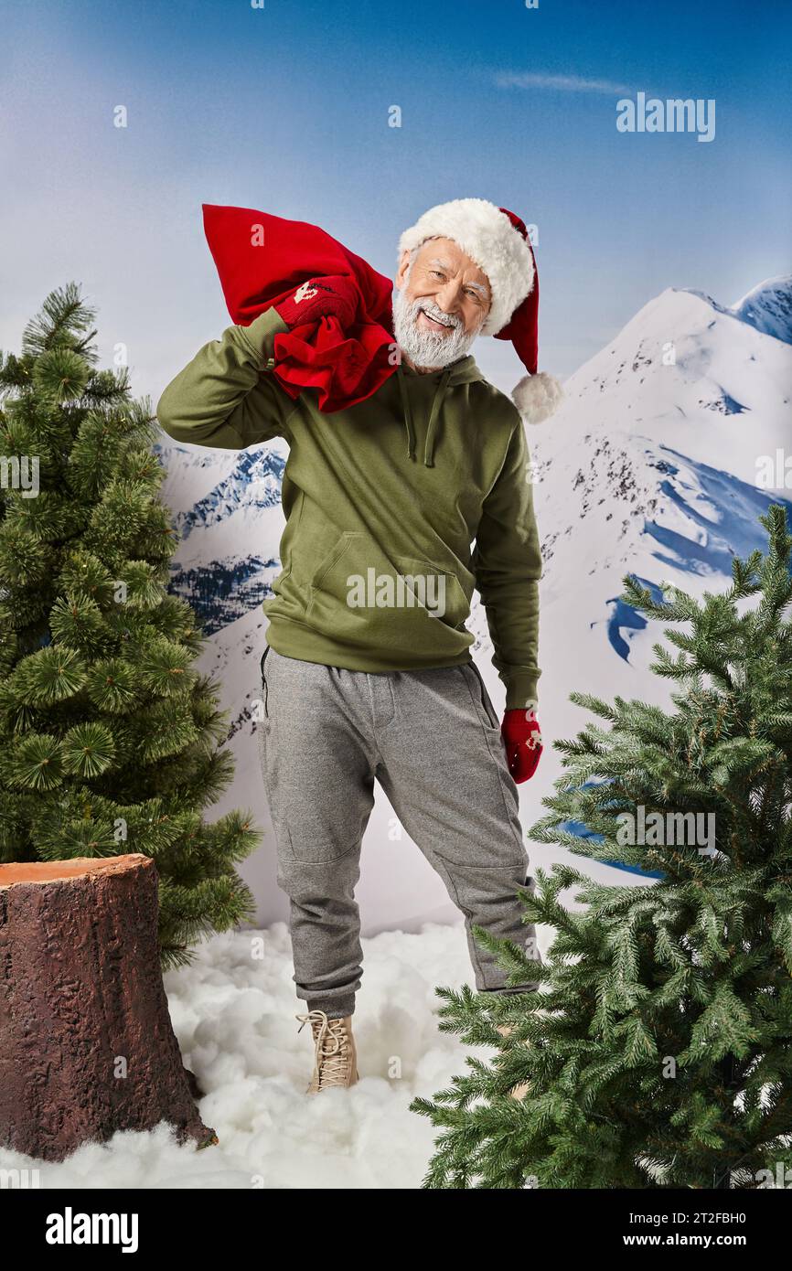 athletic Santa in warm christmassy hat and mittens holding red huge present bag, winter concept Stock Photo