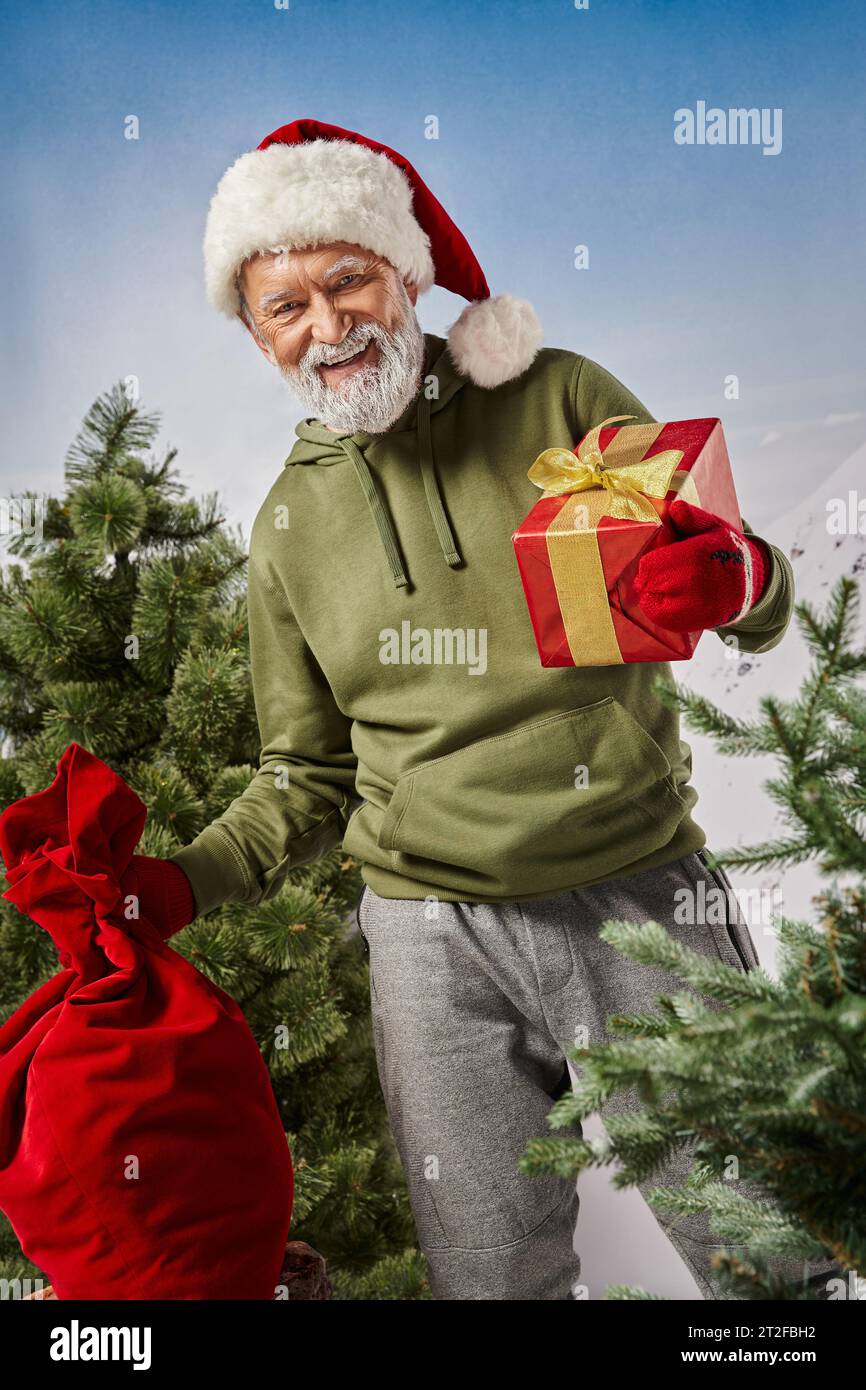 joyful Santa holding present bag and red gift in hands and smiling at camera, winter concept Stock Photo