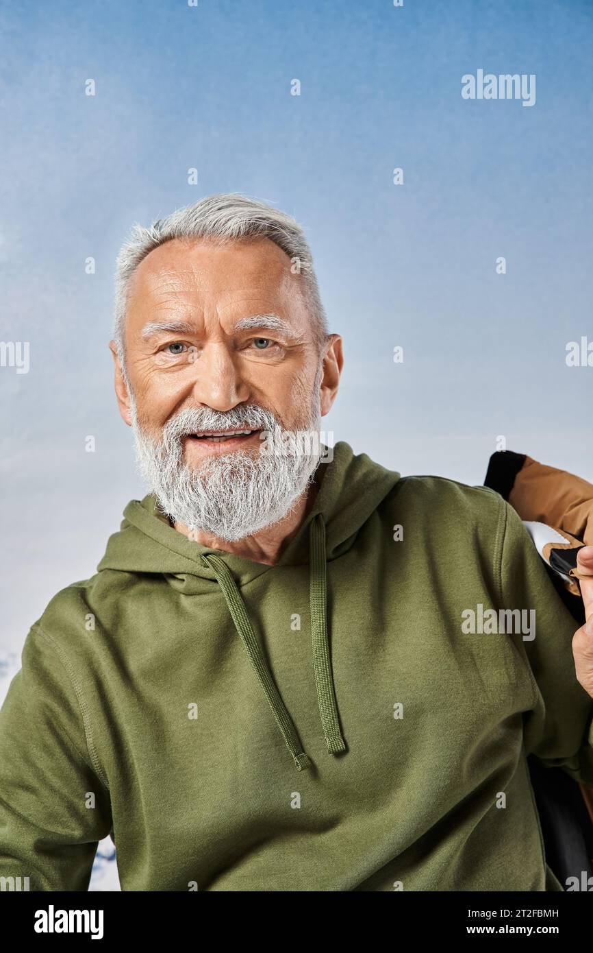 joyous Santa with white beard looking at camera with snowy mountain on backdrop, winter concept Stock Photo