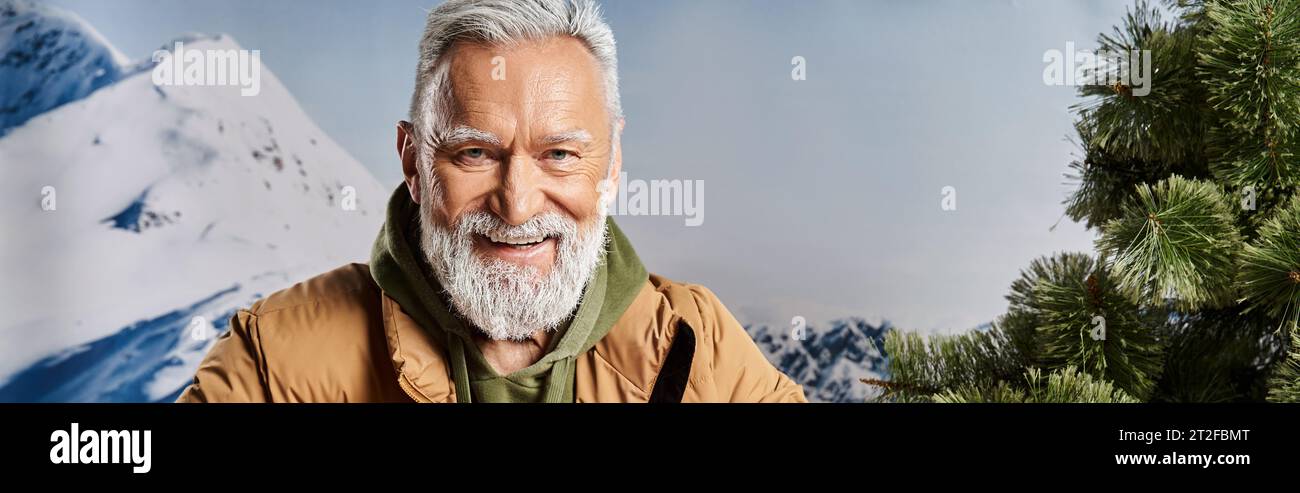 joyful Santa with white beard smiling at camera with mountains backdrop, winter concept, banner Stock Photo