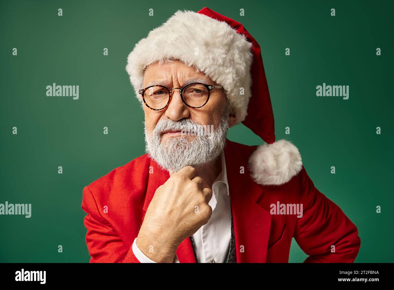 serious man dressed as Santa looking straight at camera with hand under chin, winter concept Stock Photo