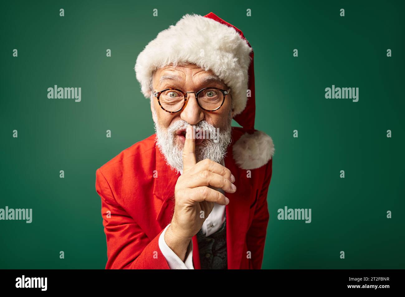 stylish Santa in red hat and glasses showing silence gesture looking at camera, winter concept Stock Photo