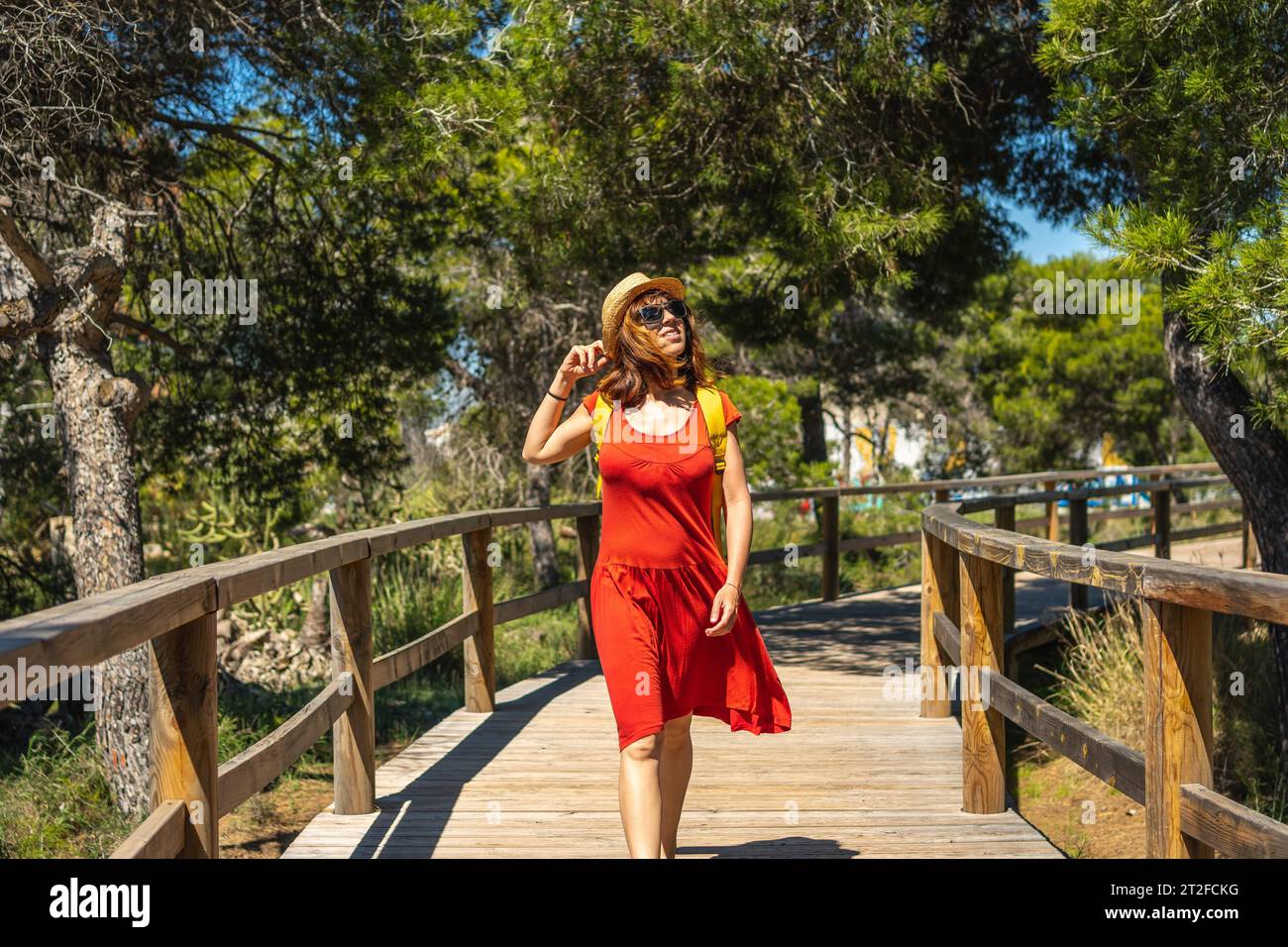 A young woman in a red dress walking along the wooden walkway towards Moncayo Beach in Guardamar del Segura, Alicante. Community of Valencia. Spain Stock Photo