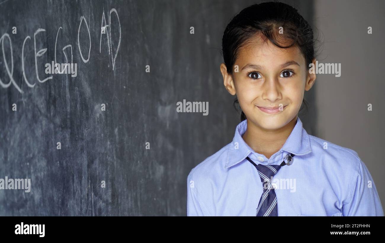 Happy Indian school girl child standing  in front of black chalkboard background. Education Concept or Back to School Stock Photo