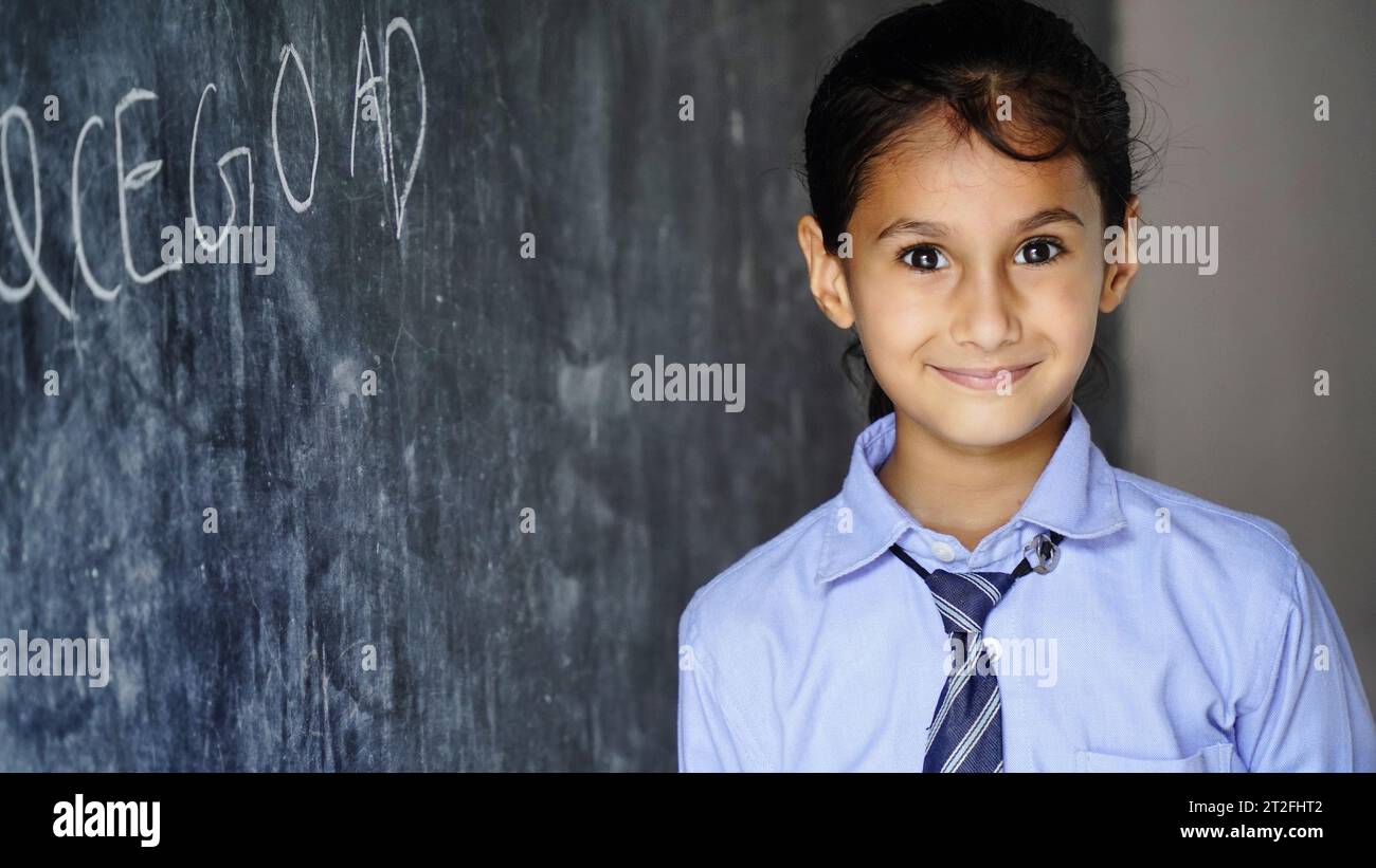 Happy Indian school girl child standing in front of black chalkboard