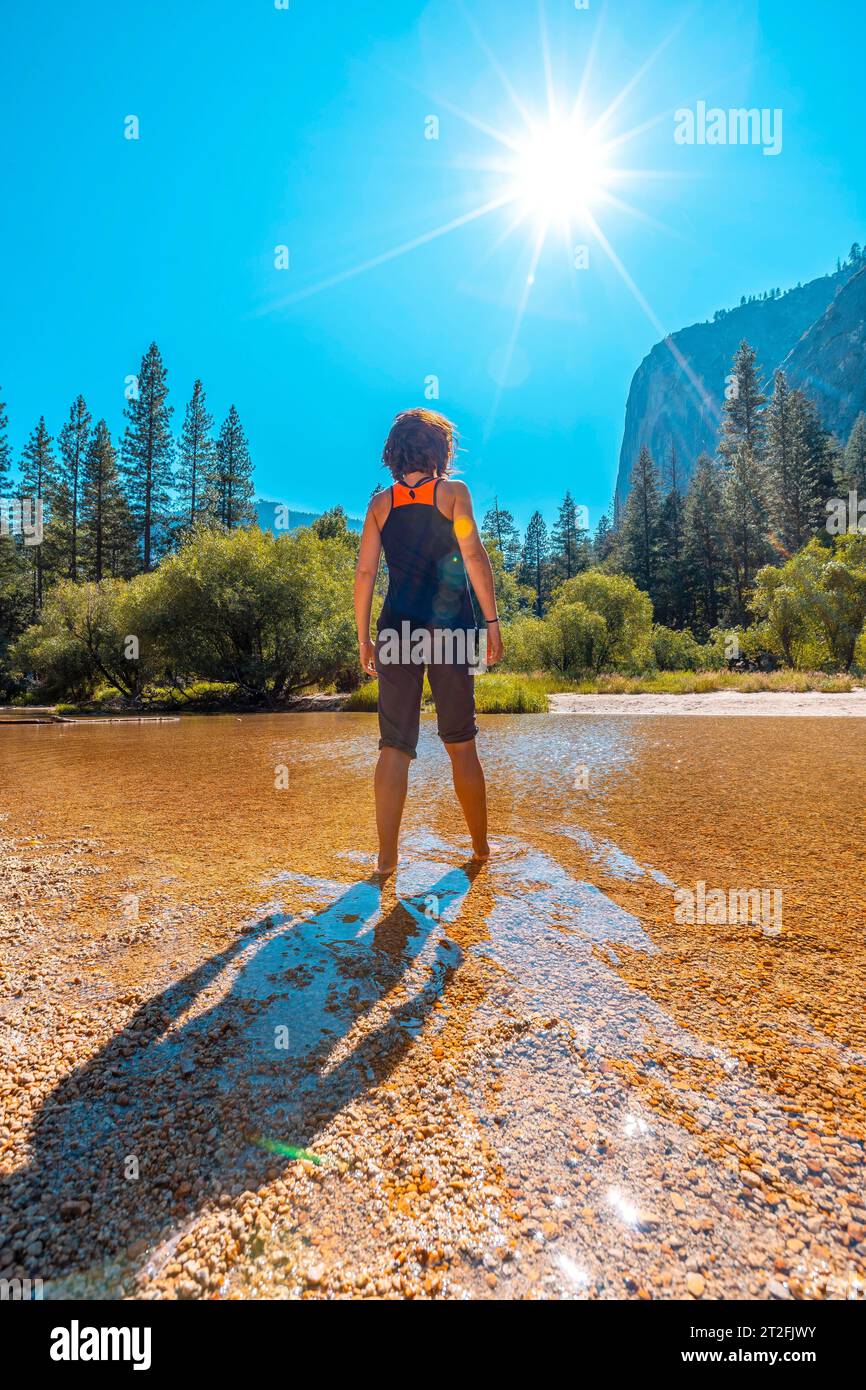 Mirror lake, a young woman with black t-shirt in the lake water and the sun in the background. California, United States Stock Photo