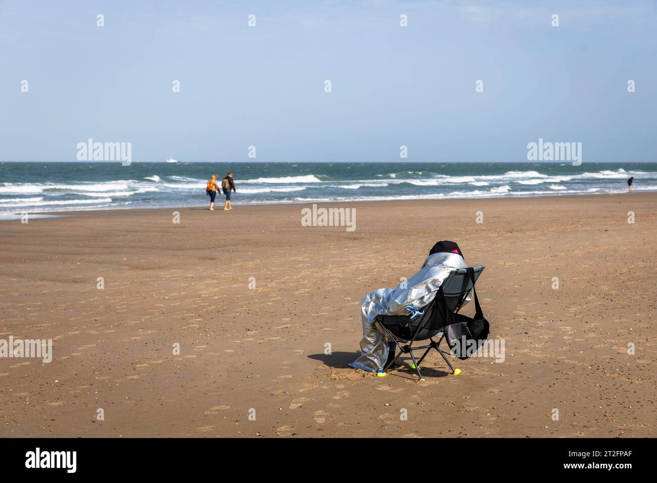 person sits wrapped in an insulating blanket on the beach near Domburg on the peninsula Walcheren, Zeeland, Netherlands. Person sitzt eingehuellt in e Stock Photo