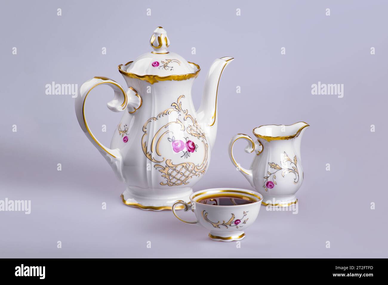 Ancient German faience tea (coffee) service with a kettle, a milk cup and a cup filled with tea (coffee) on a gray-gray background Stock Photo