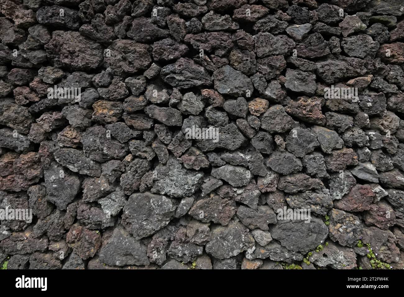 A wall made up of dark, volcanic pumice rocks is shown in a closeup, exterior view during the day. Stock Photo