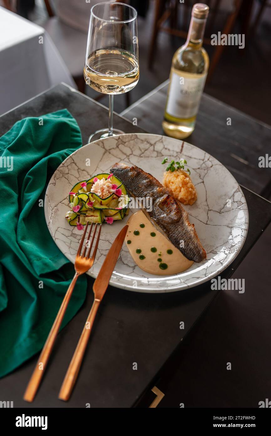 Sea bass or dorado fillet with baked zucchini and sauce on a gray plate in a restaurant Stock Photo