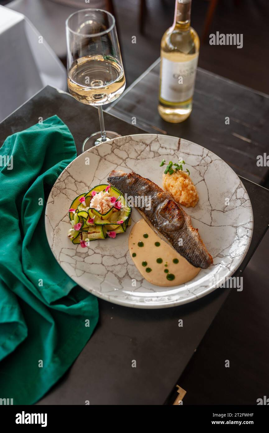 Sea bass or dorado fillet with baked zucchini and sauce on a gray plate in a restaurant Stock Photo