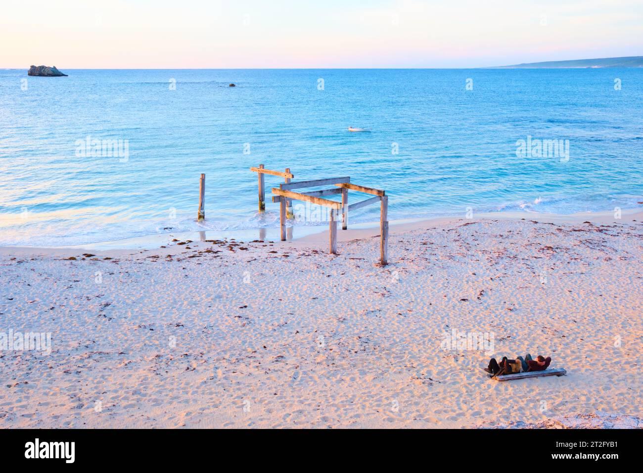 Remains of the old jetty and two people watching the sunset at Hamelin Bay in the south-west region of Western Australia. Stock Photo