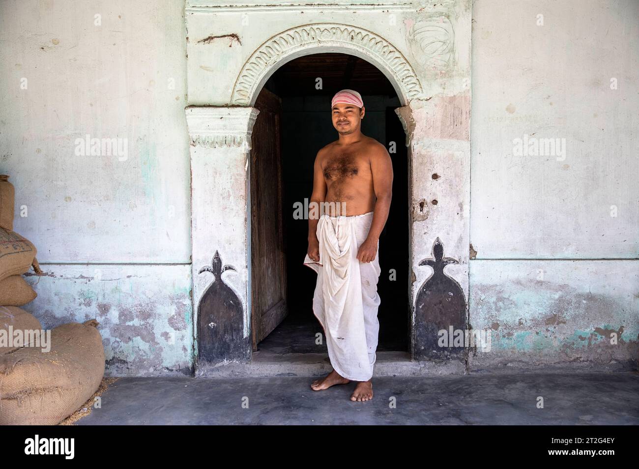 Hindu monk in traditional clothes standing at the entrance of the Uttar Kamalabari Hindu monastery, Majuli Island, Assam, India Stock Photo