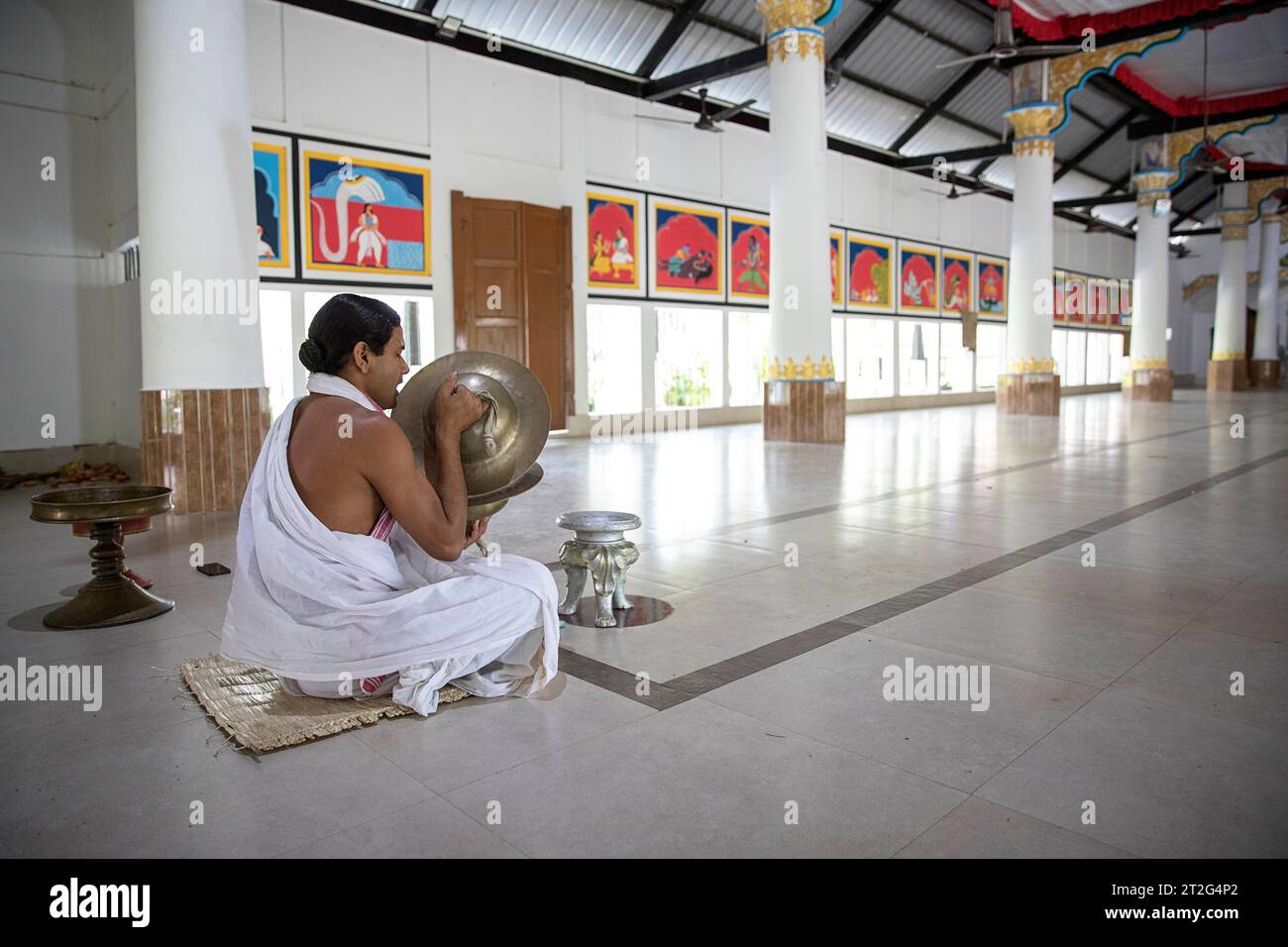 Hindu monk sitting on the floor at the Uttar Kamalabari Hindu monastery, praying and playing on cymbals, Majuli Island, India Stock Photo