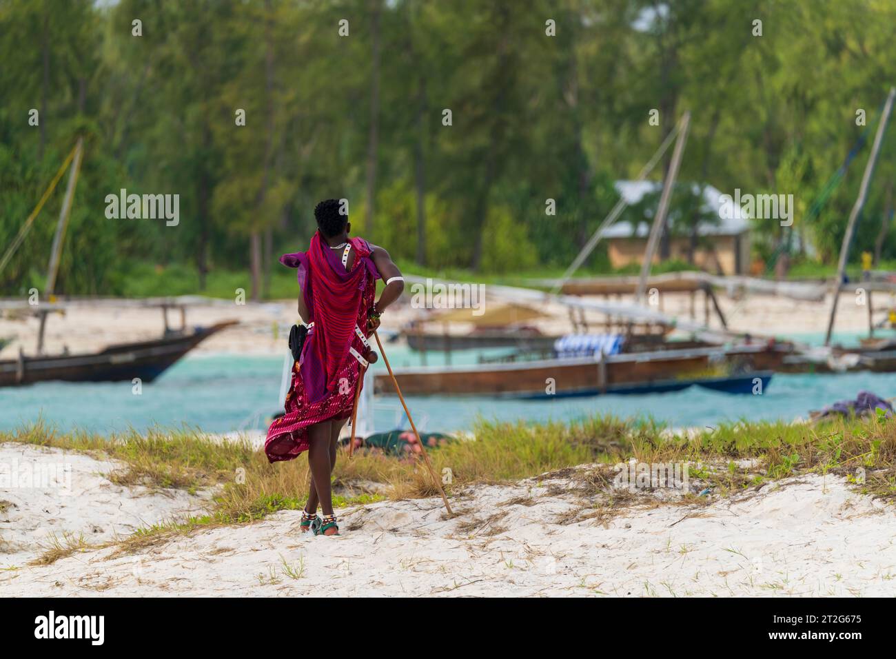View from behind of a Zanzibar Masai dressed in traditional clothing as he stands looking at the sea at sunny day, zanzibar , Tanzania Stock Photo