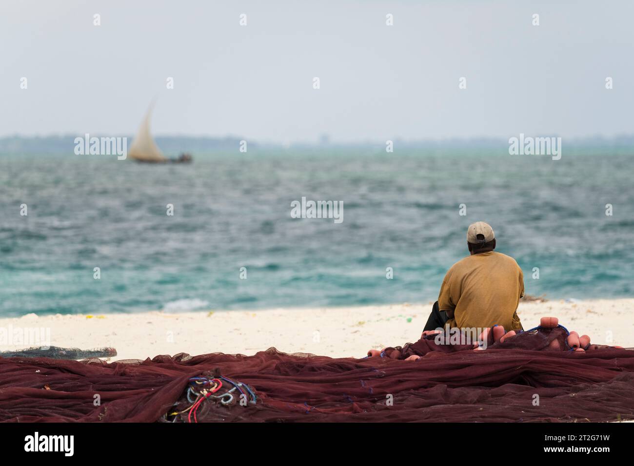 African fisherman sitting on fishing nets looks out to sea, overcast day, Zanzibar , Tanzania. Stock Photo