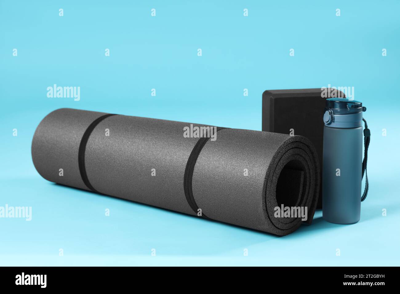 Exercise mat, yoga block and bottle of water on light blue background ...