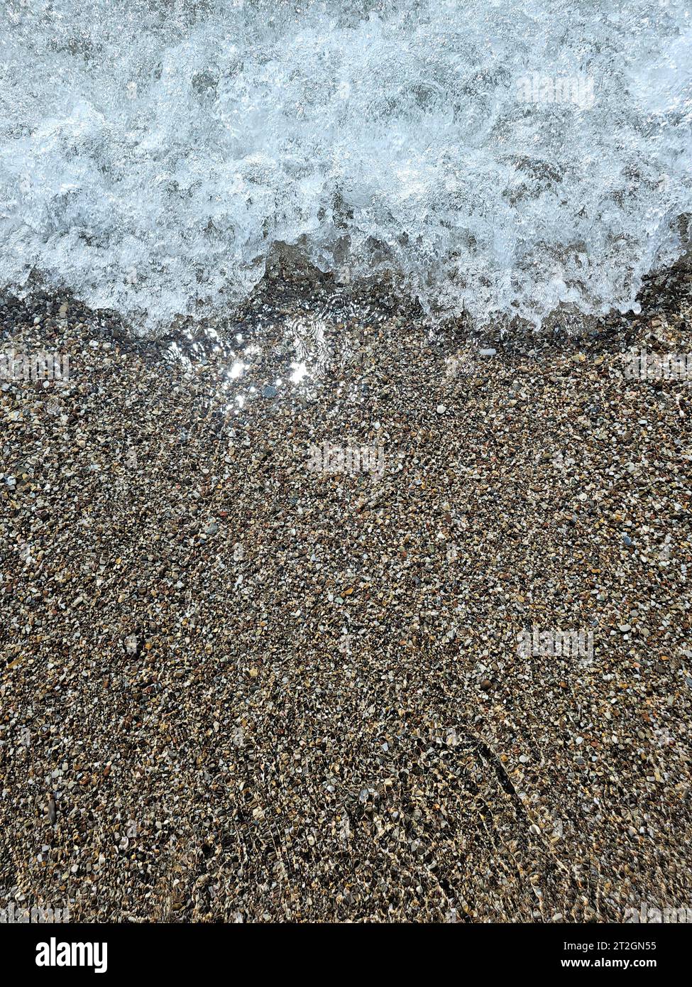 Directly above view on a wave rolling over colorful pebbles on a beach. Stock Photo