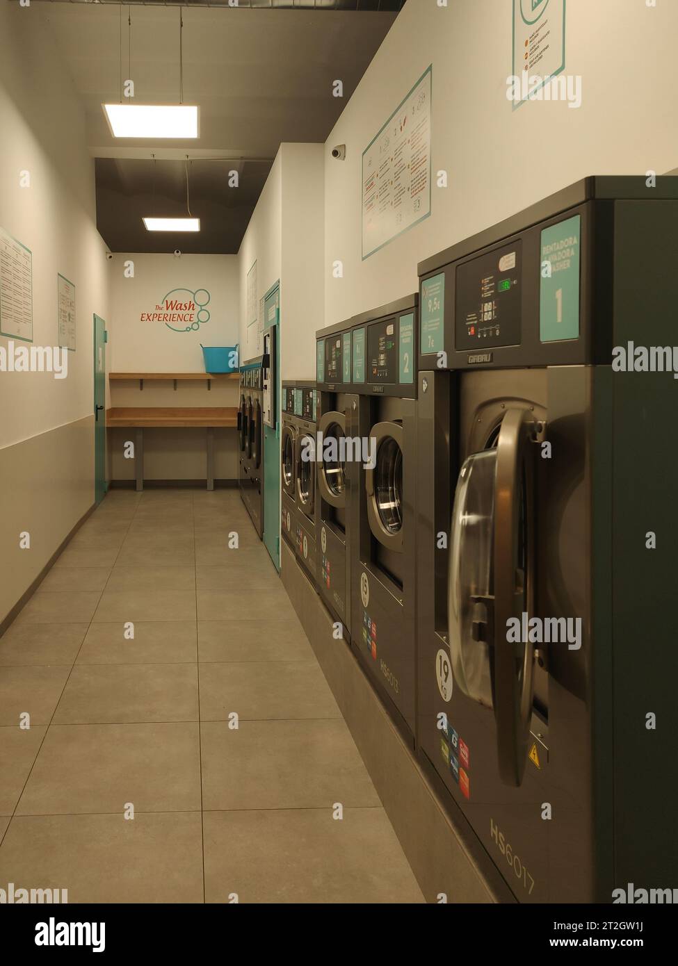 Detail of a small self-service laundry, it is narrow in the form of a corridor and there are several washers and dryers Stock Photo