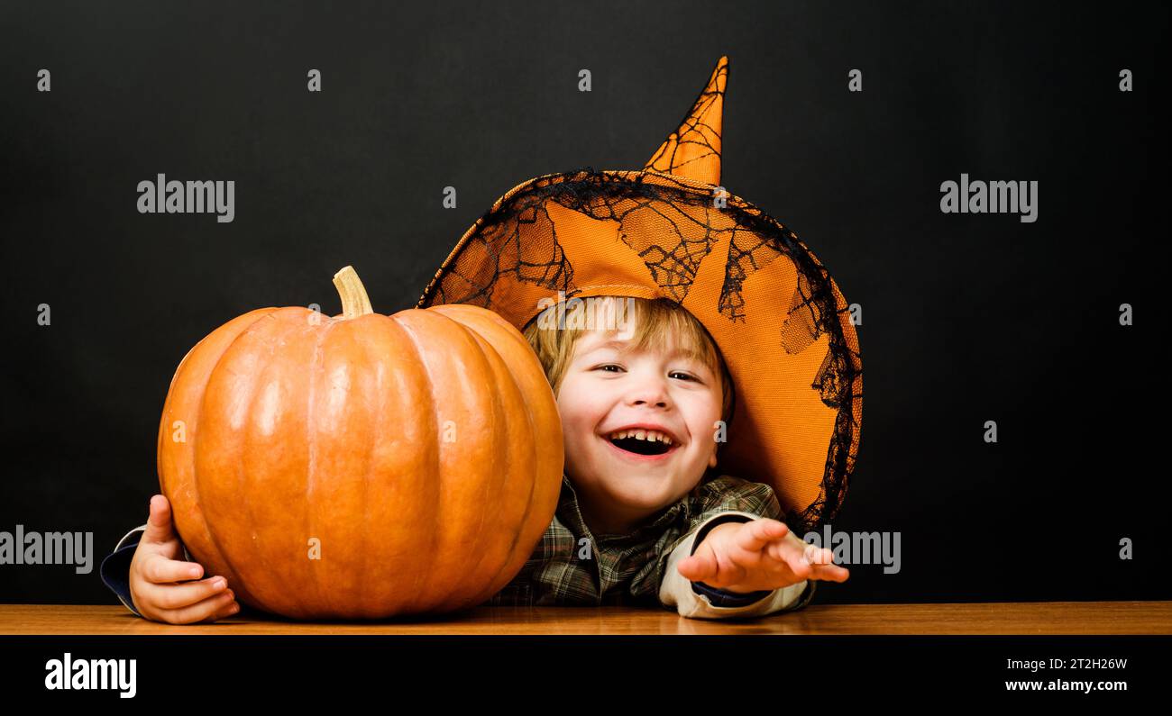 Happy Halloween holidays. Funny child in witch hat with pumpkin for Halloween. Toddler kid with jack-o-lantern. Trick or treat. Smiling little boy in Stock Photo