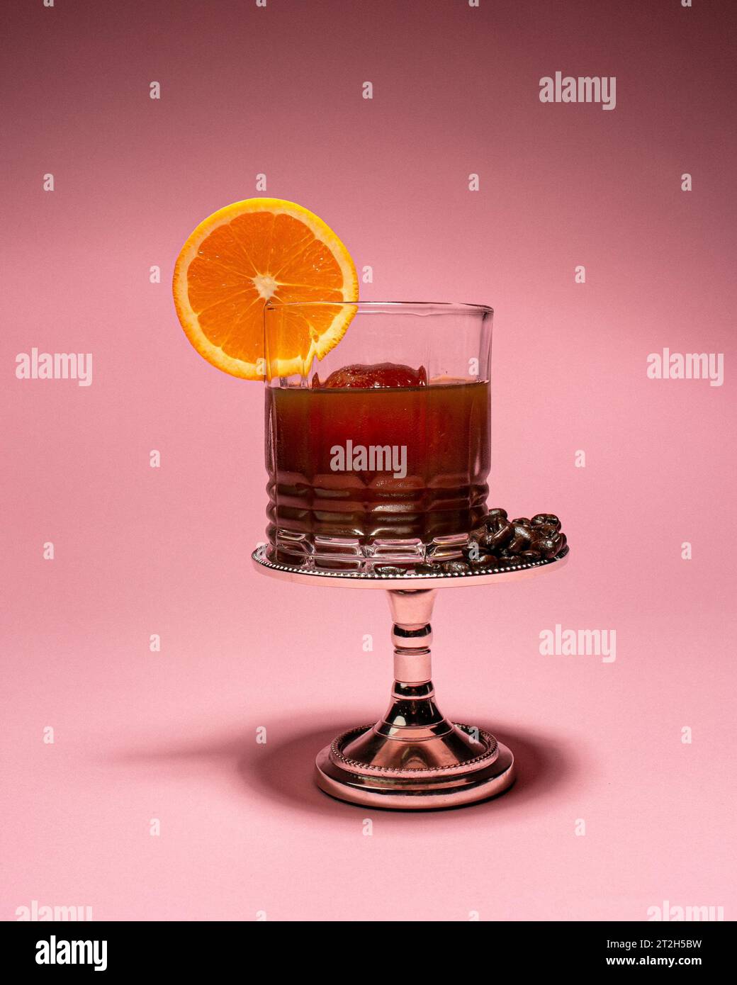 A refreshing cocktail with an orange slice garnish atop a silver stand ...