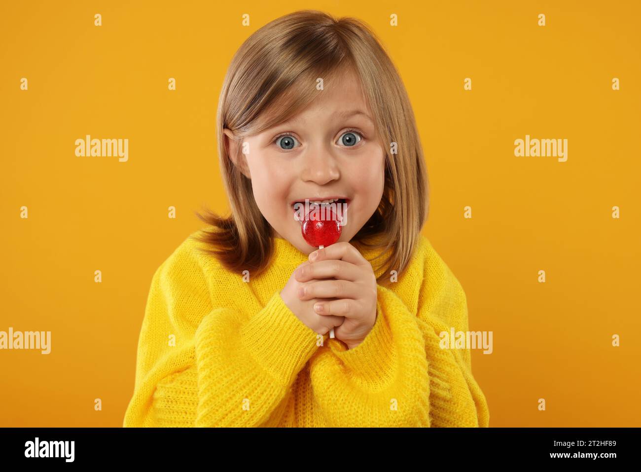 Excited girl licking lollipop on orange background Stock Photo